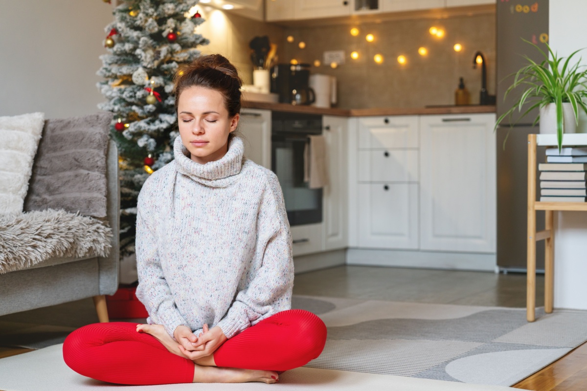 A woman wearing jacket and red pants meditating with Christmas tree at the background